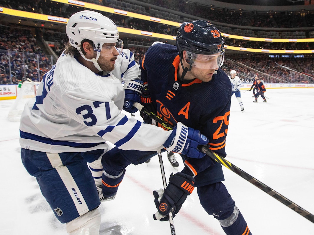 Timothy Liljegren von den Toronto Maple Leafs und Leon Draisaitl von den Edmonton Oilers befinden sich im Zweikampf, obwohl der Puck noch in der Ferne ist.