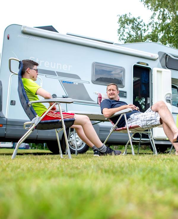 Zwei Männer sitzen auf dem Campingplatz am Birkensee vor ihrem Wohnmobil.