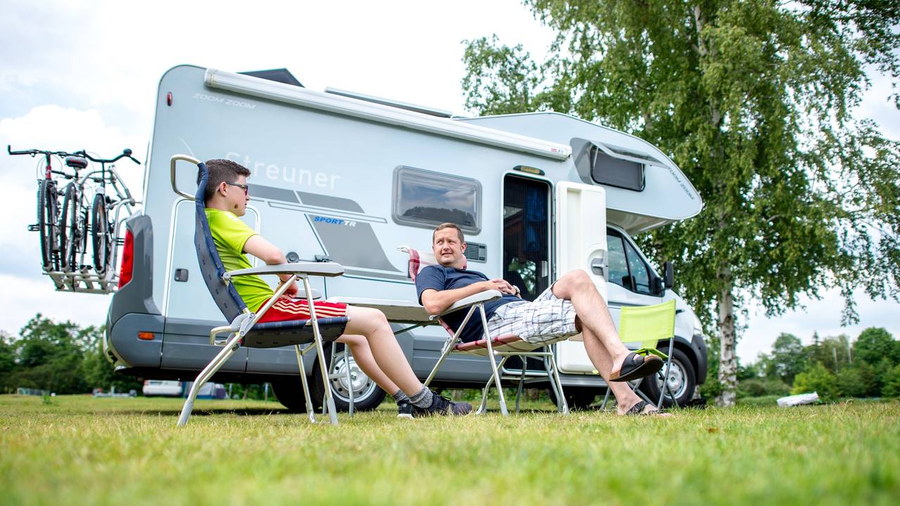 Zwei Männer sitzen auf dem Campingplatz am Birkensee vor ihrem Wohnmobil.