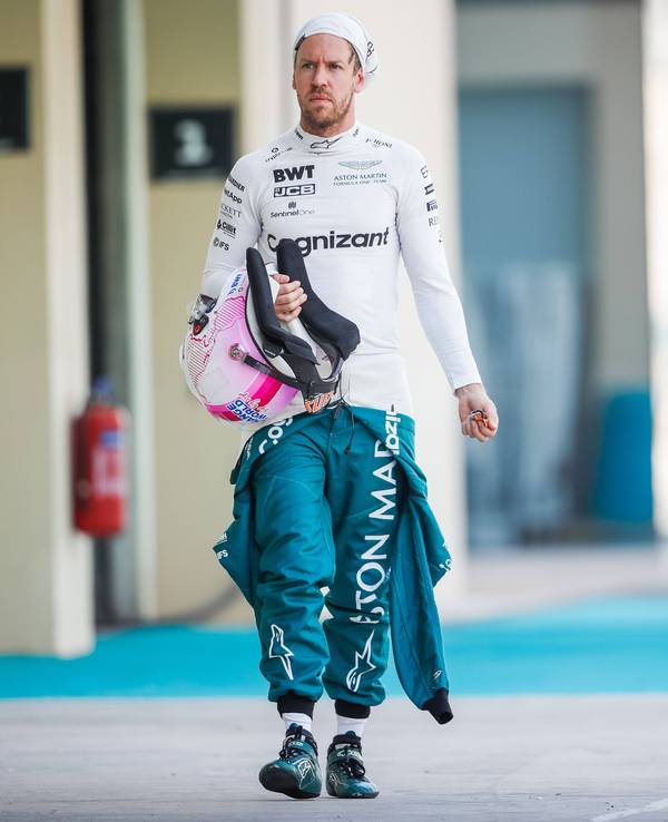 Sebastian Vettel hat seinen Schutzanzug halb ausgezogen, in der Hand hält er seinen Helm. Die Feuermaske trägt er hochgezogen.
