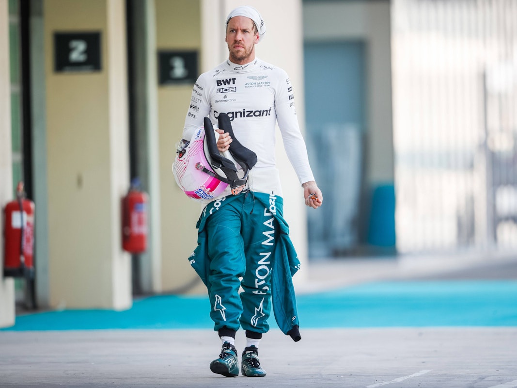 Sebastian Vettel hat seinen Schutzanzug halb ausgezogen, in der Hand hält er seinen Helm. Die Feuermaske trägt er hochgezogen.