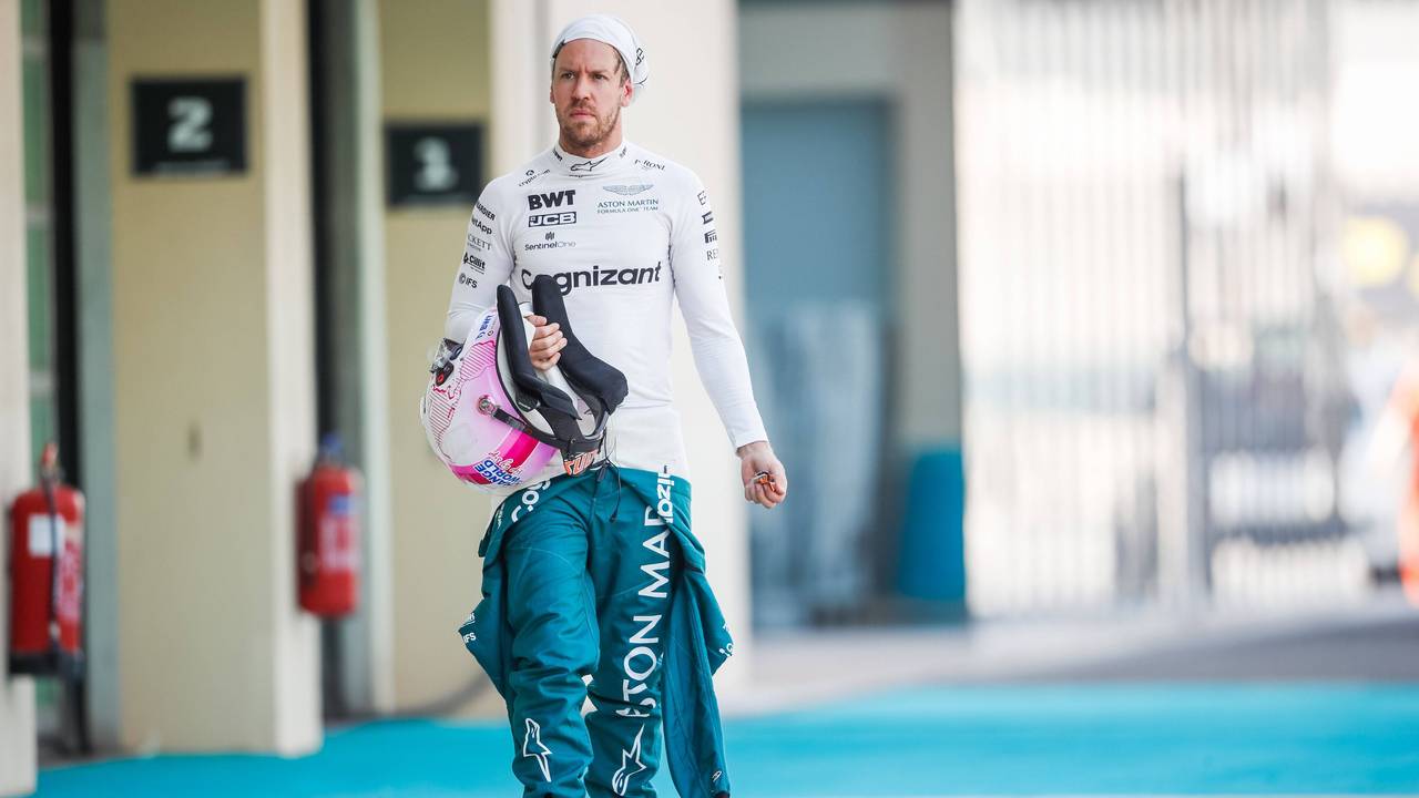 Sebastian Vettel hat seinen Schutzanzug halb ausgezogen, in der Hand hält er seinen Helm. Die Feuermaske trägt er hochgezogen.