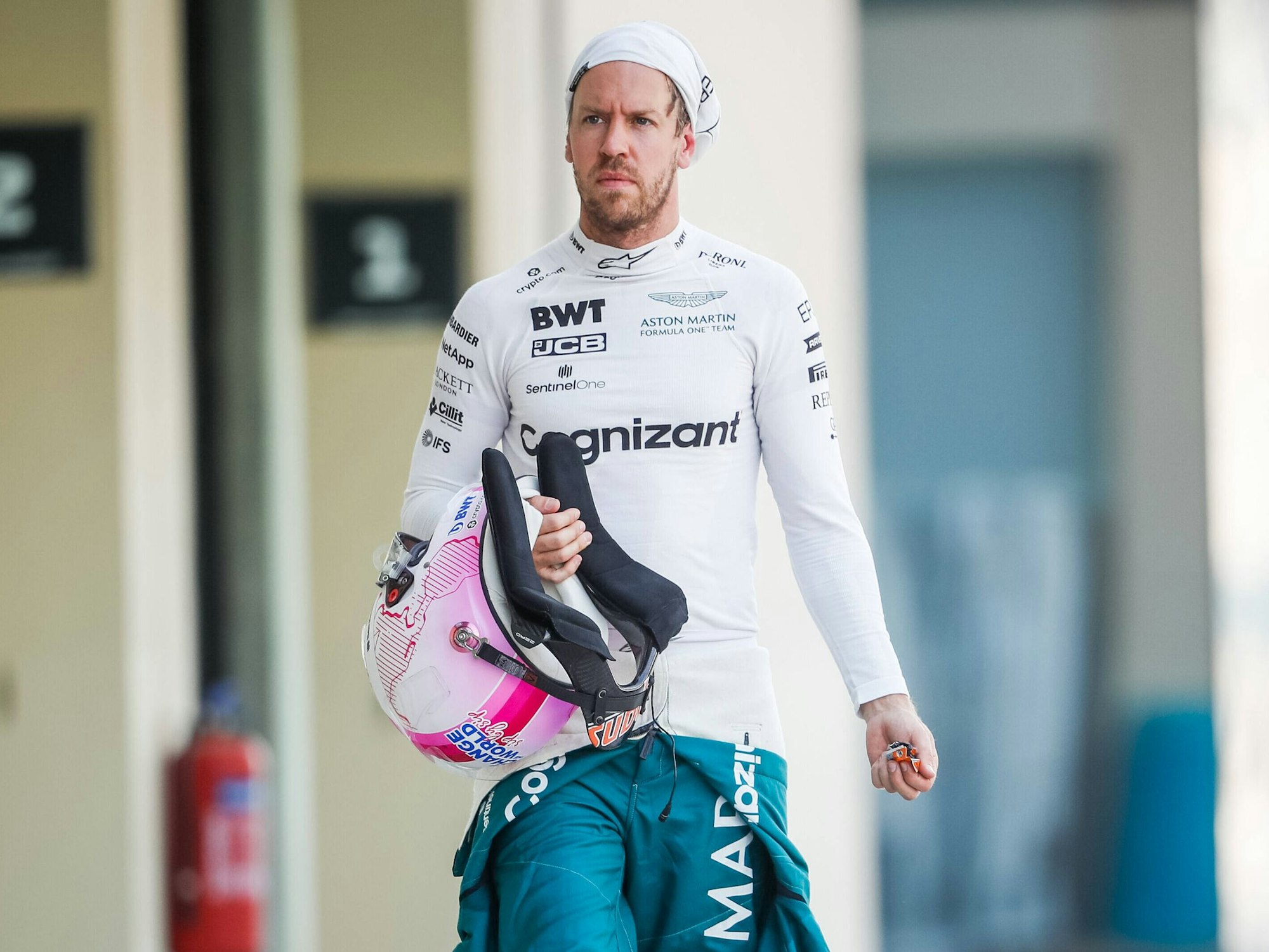 Sebastian Vettel hat seinen Schutzanzug halb ausgezogen, in der Hand hält er seinen Helm. Die Feuermaske trägt er hochgezogen.