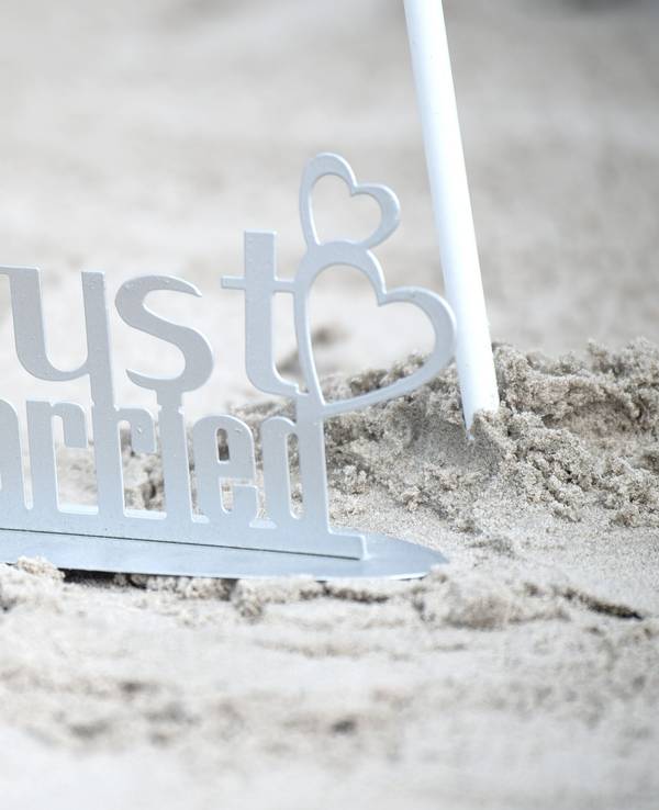 Ein weißer „Just Married“-Metallaufsteller im Sand.