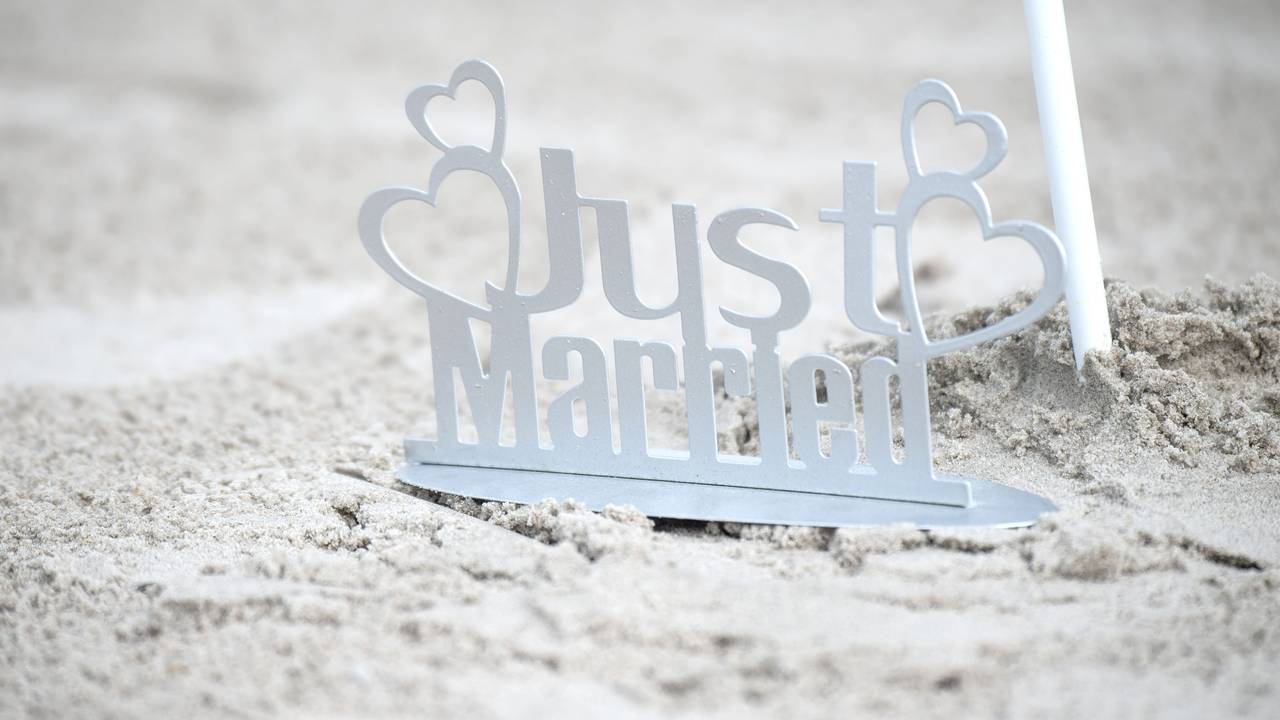 Ein weißer „Just Married“-Metallaufsteller im Sand.
