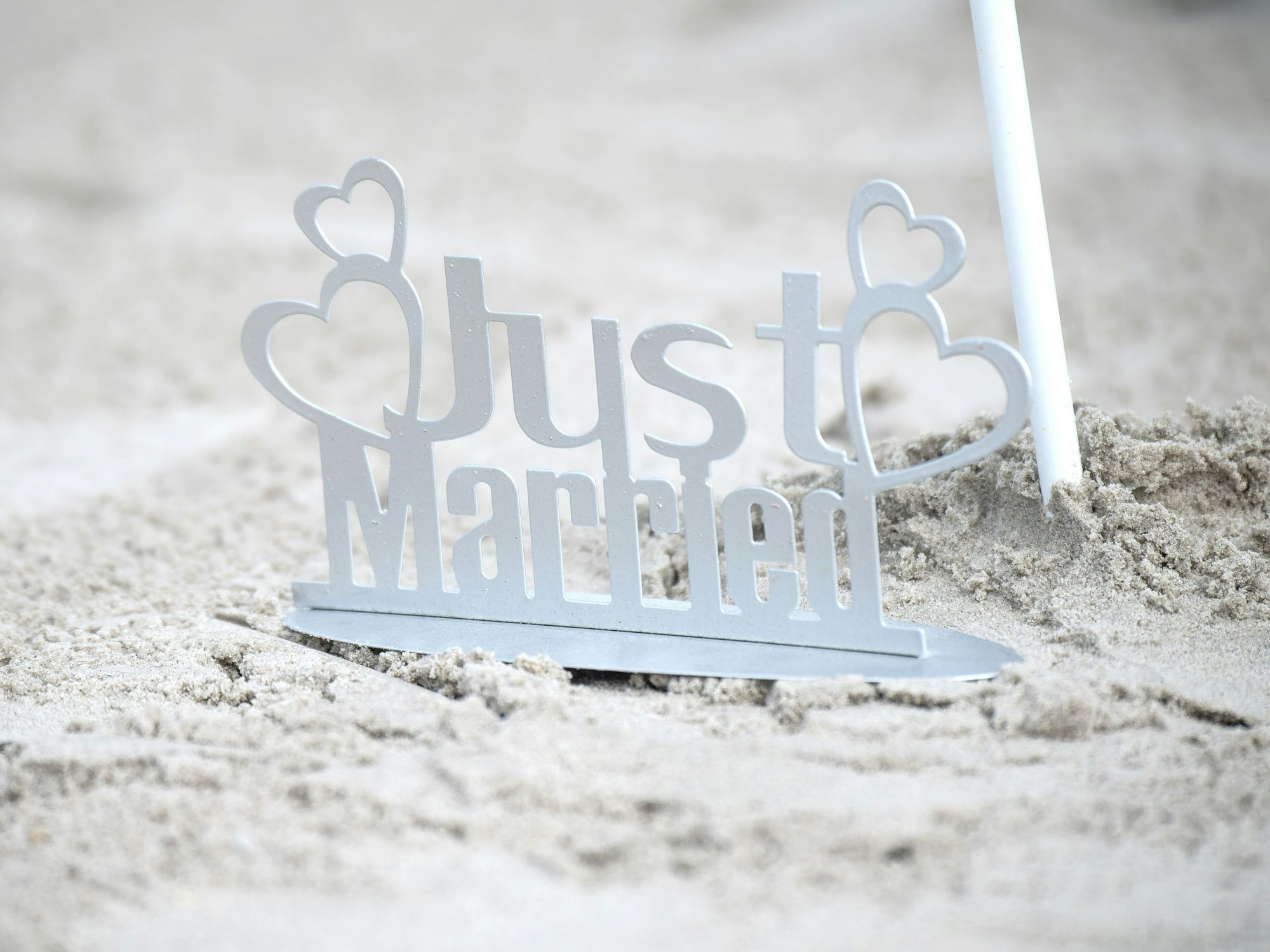 Ein weißer „Just Married“-Metallaufsteller im Sand.