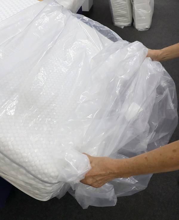 Eine Frau packt in einem Fachgeschäft für Matratzen eine neue Matratze aus der Verpackungsfolie aus.