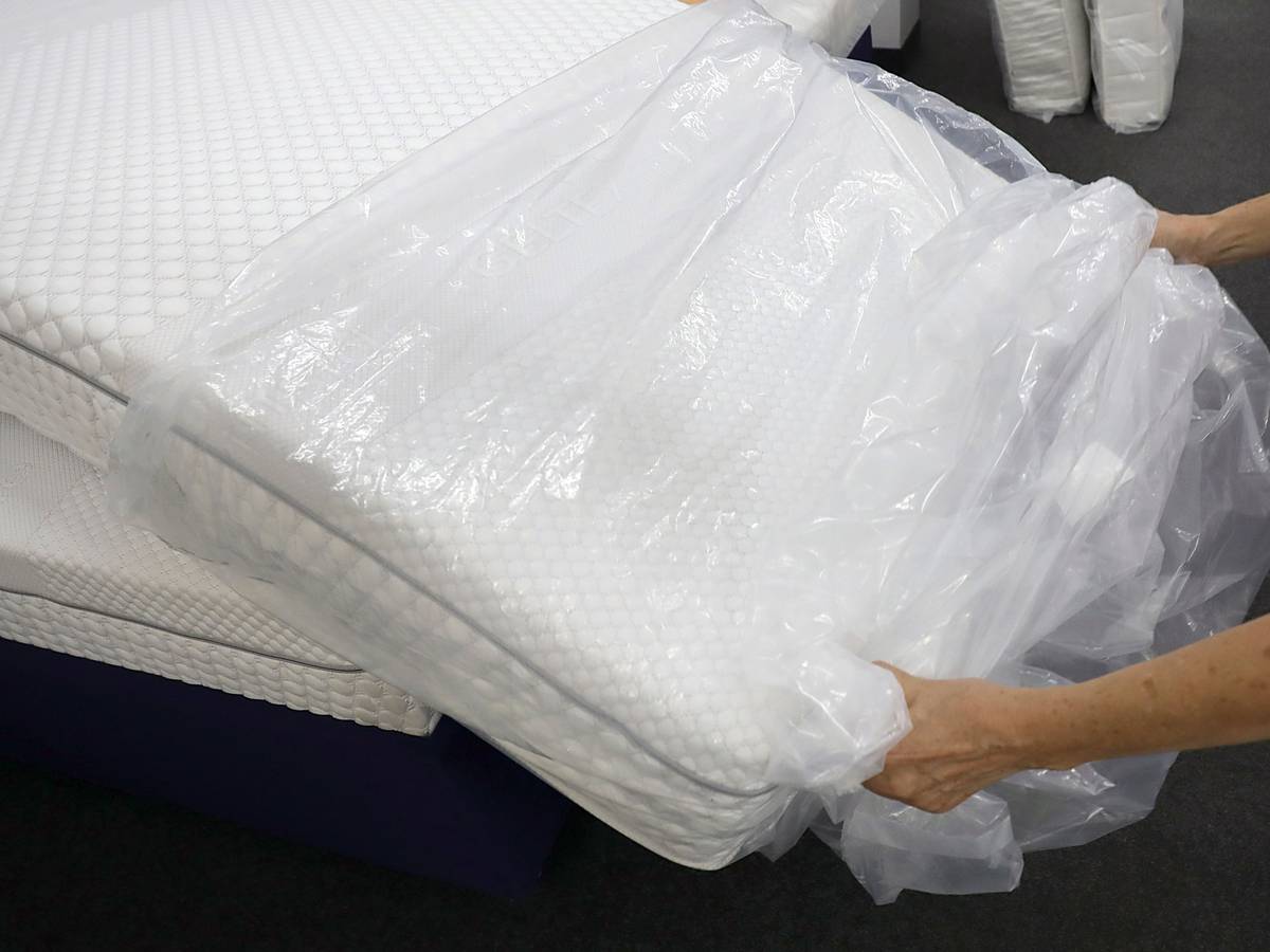 Eine Frau packt in einem Fachgeschäft für Matratzen eine neue Matratze aus der Verpackungsfolie aus.