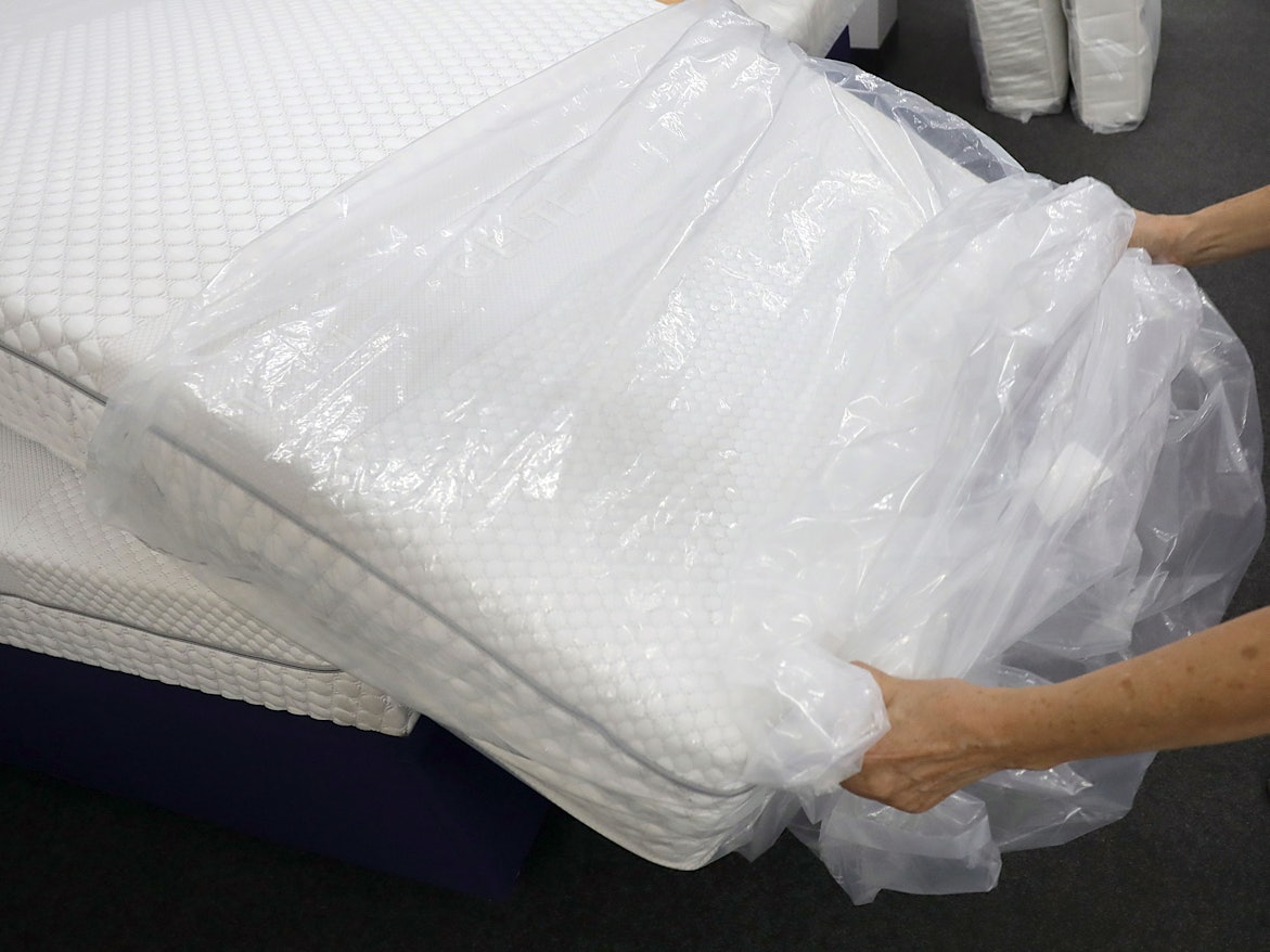 Eine Frau packt in einem Fachgeschäft für Matratzen eine neue Matratze aus der Verpackungsfolie aus.