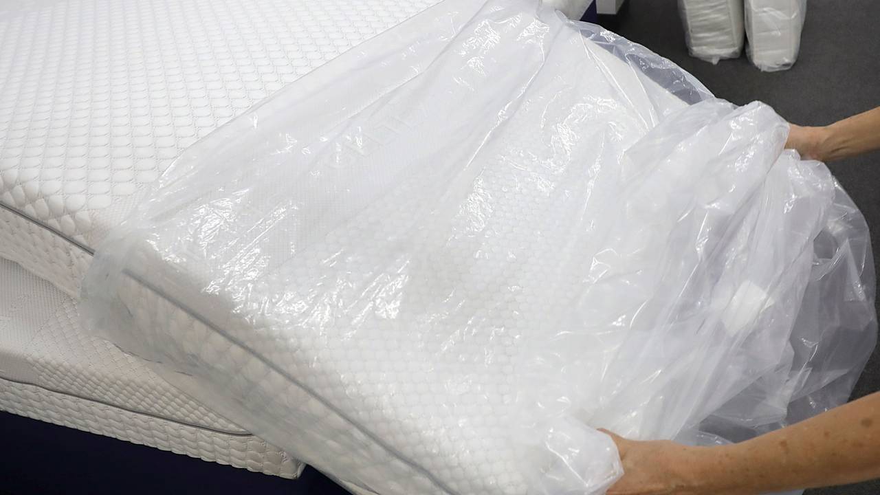 Eine Frau packt in einem Fachgeschäft für Matratzen eine neue Matratze aus der Verpackungsfolie aus.