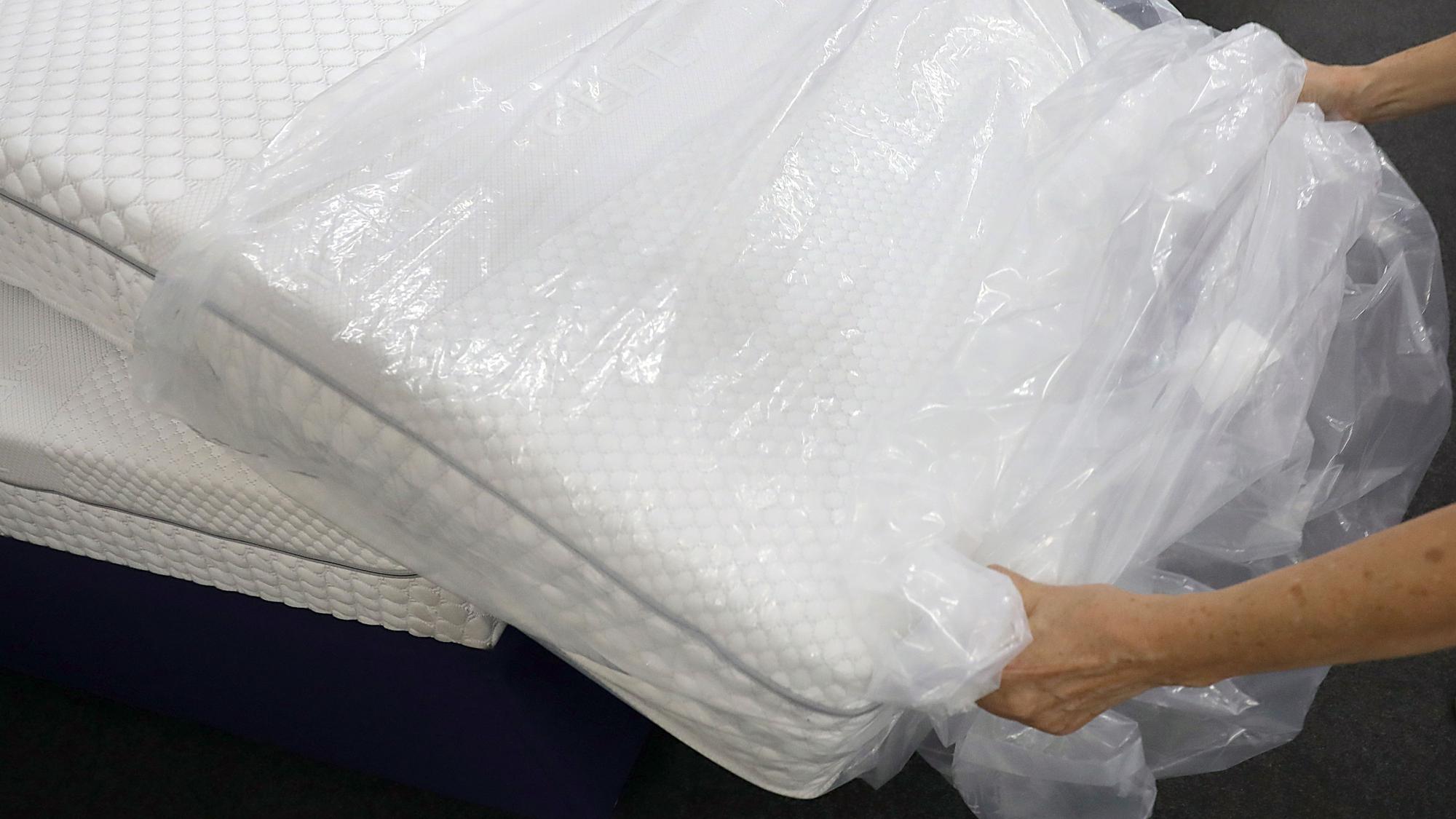Eine Frau packt in einem Fachgeschäft für Matratzen eine neue Matratze aus der Verpackungsfolie aus.