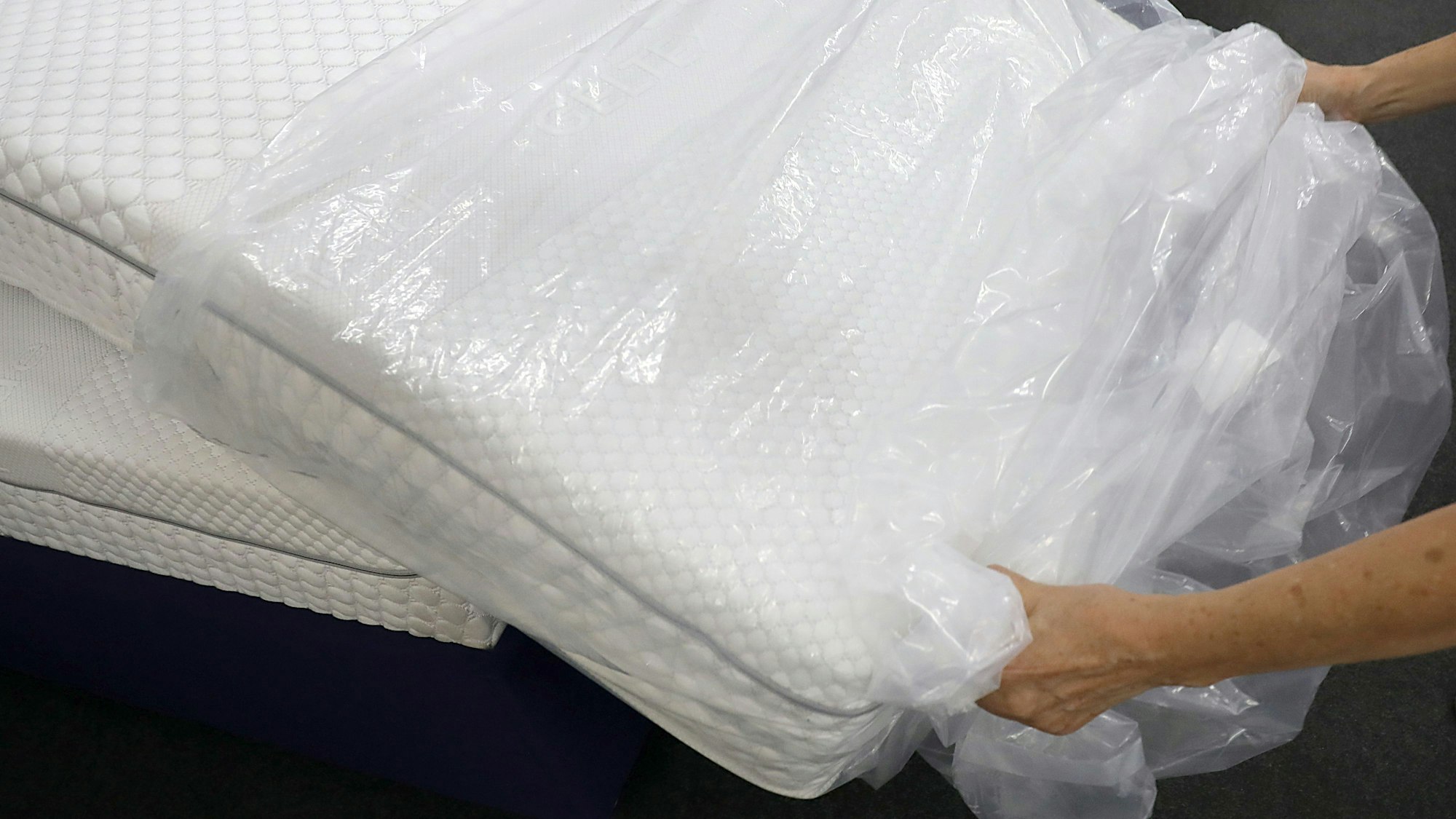 Eine Frau packt in einem Fachgeschäft für Matratzen eine neue Matratze aus der Verpackungsfolie aus.