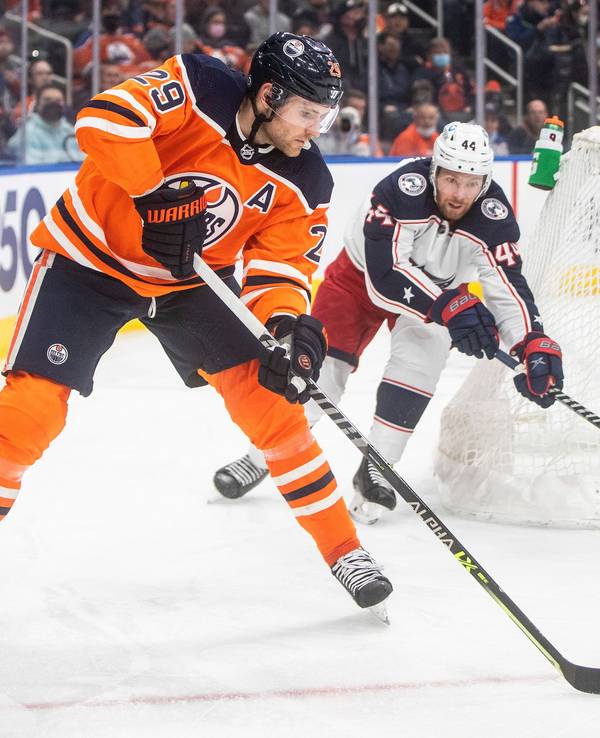 NHL-Star Leon Draisaitl (l.) schlittert hinter dem Tor von Kraken-Goalie Elvis Merzlikins (r.) vorbei und wird von Kraken-Profi Vladislav Gavrikov (M.) verfolgt.
