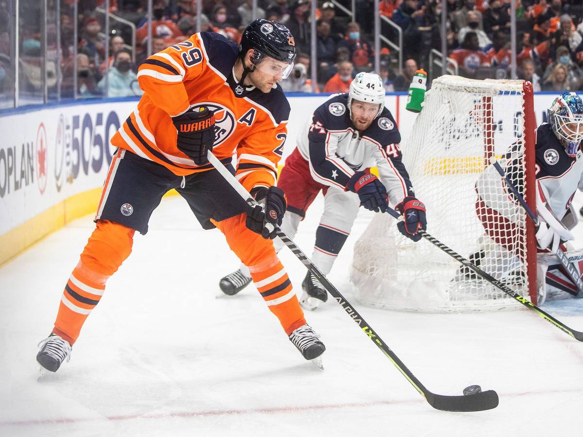 NHL-Star Leon Draisaitl (l.) schlittert hinter dem Tor von Kraken-Goalie Elvis Merzlikins (r.) vorbei und wird von Kraken-Profi Vladislav Gavrikov (M.) verfolgt.