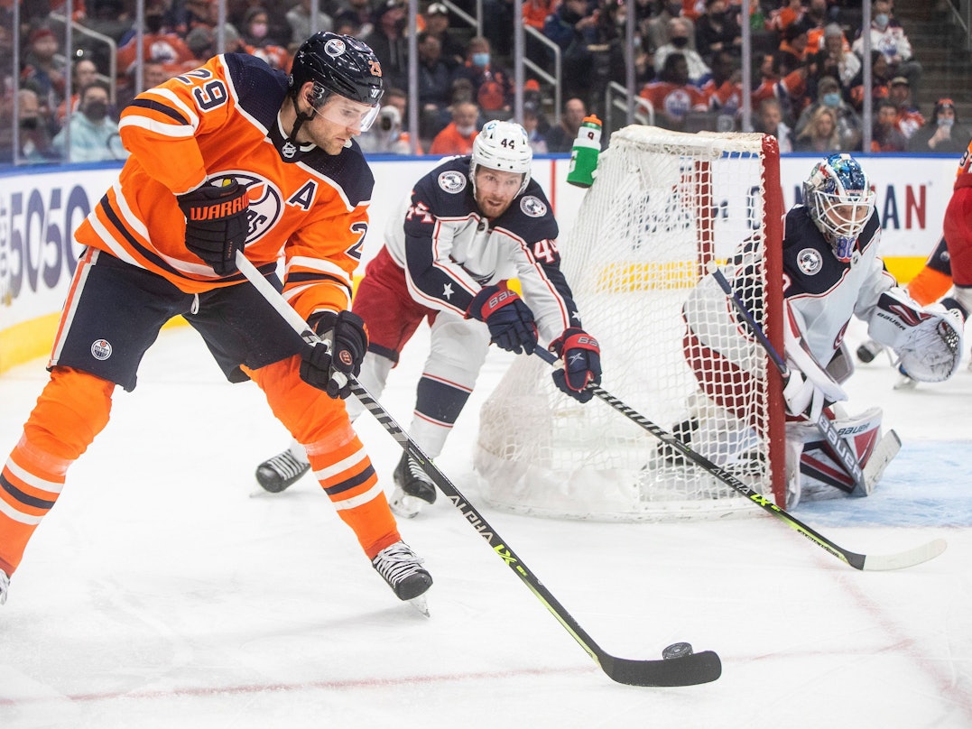 NHL-Star Leon Draisaitl (l.) schlittert hinter dem Tor von Kraken-Goalie Elvis Merzlikins (r.) vorbei und wird von Kraken-Profi Vladislav Gavrikov (M.) verfolgt.