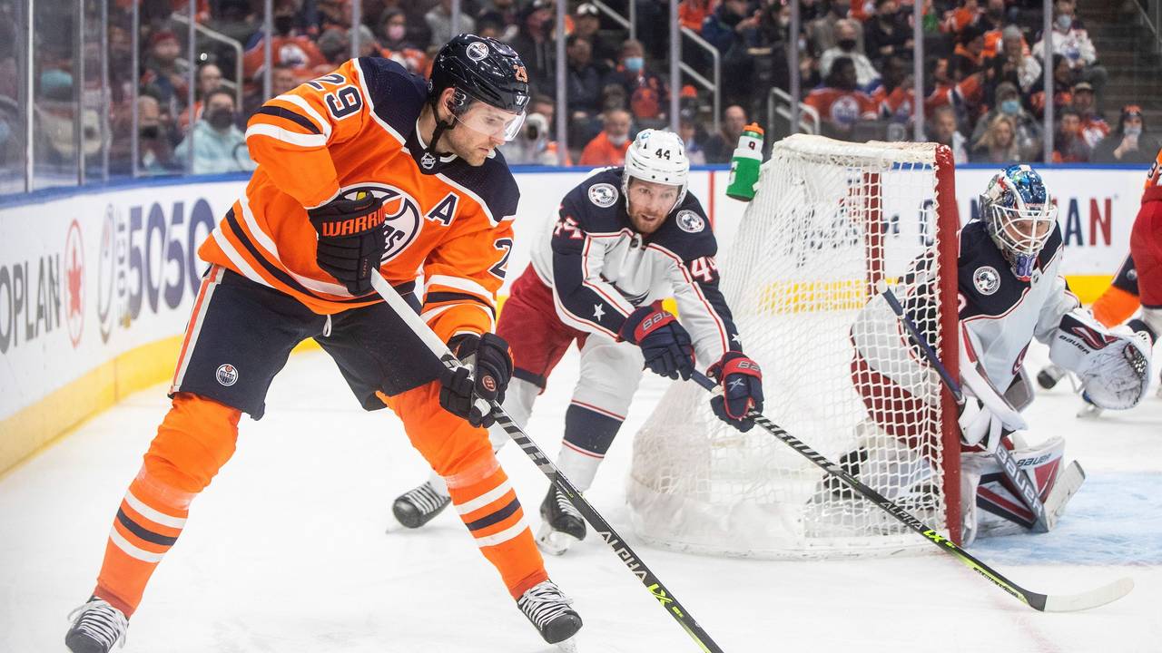 NHL-Star Leon Draisaitl (l.) schlittert hinter dem Tor von Kraken-Goalie Elvis Merzlikins (r.) vorbei und wird von Kraken-Profi Vladislav Gavrikov (M.) verfolgt.
