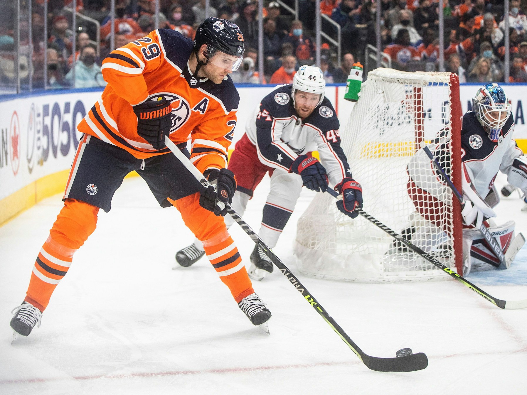 NHL-Star Leon Draisaitl (l.) schlittert hinter dem Tor von Kraken-Goalie Elvis Merzlikins (r.) vorbei und wird von Kraken-Profi Vladislav Gavrikov (M.) verfolgt.