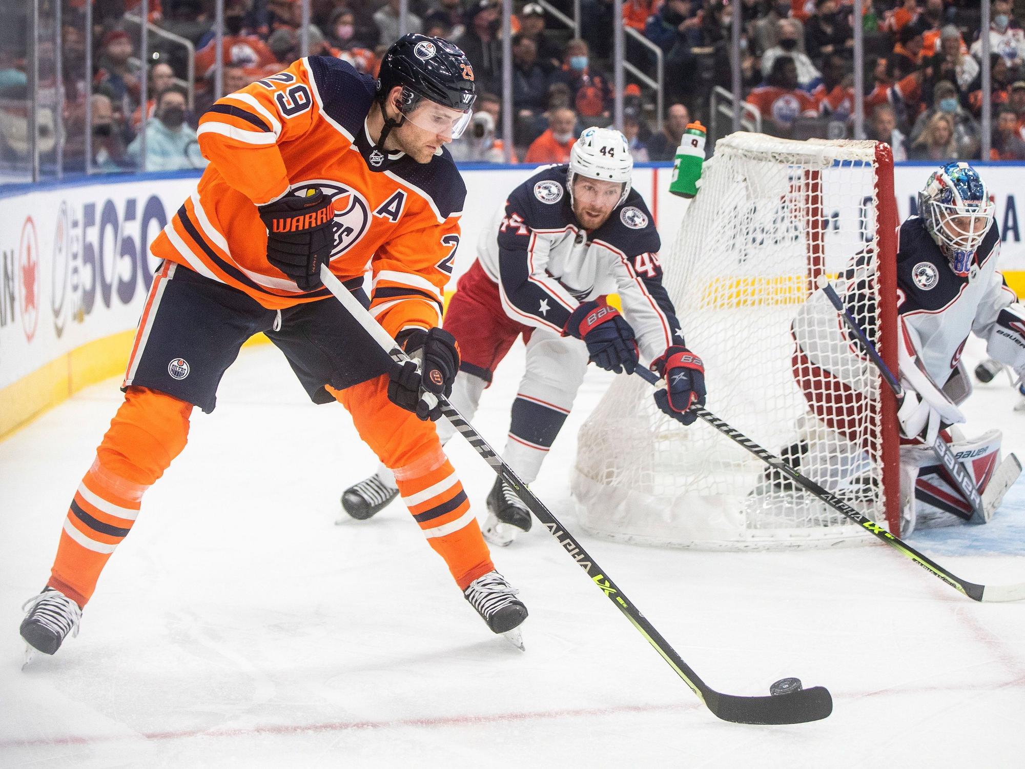 NHL-Star Leon Draisaitl (l.) schlittert hinter dem Tor von Kraken-Goalie Elvis Merzlikins (r.) vorbei und wird von Kraken-Profi Vladislav Gavrikov (M.) verfolgt.