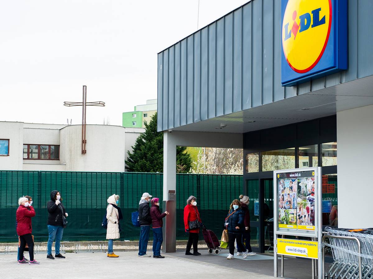 Kunden stehen mit Mundschutz und unter Einhaltung eines Sicherheitsabstandes vor einem Lidl Supermarkt Schlange.