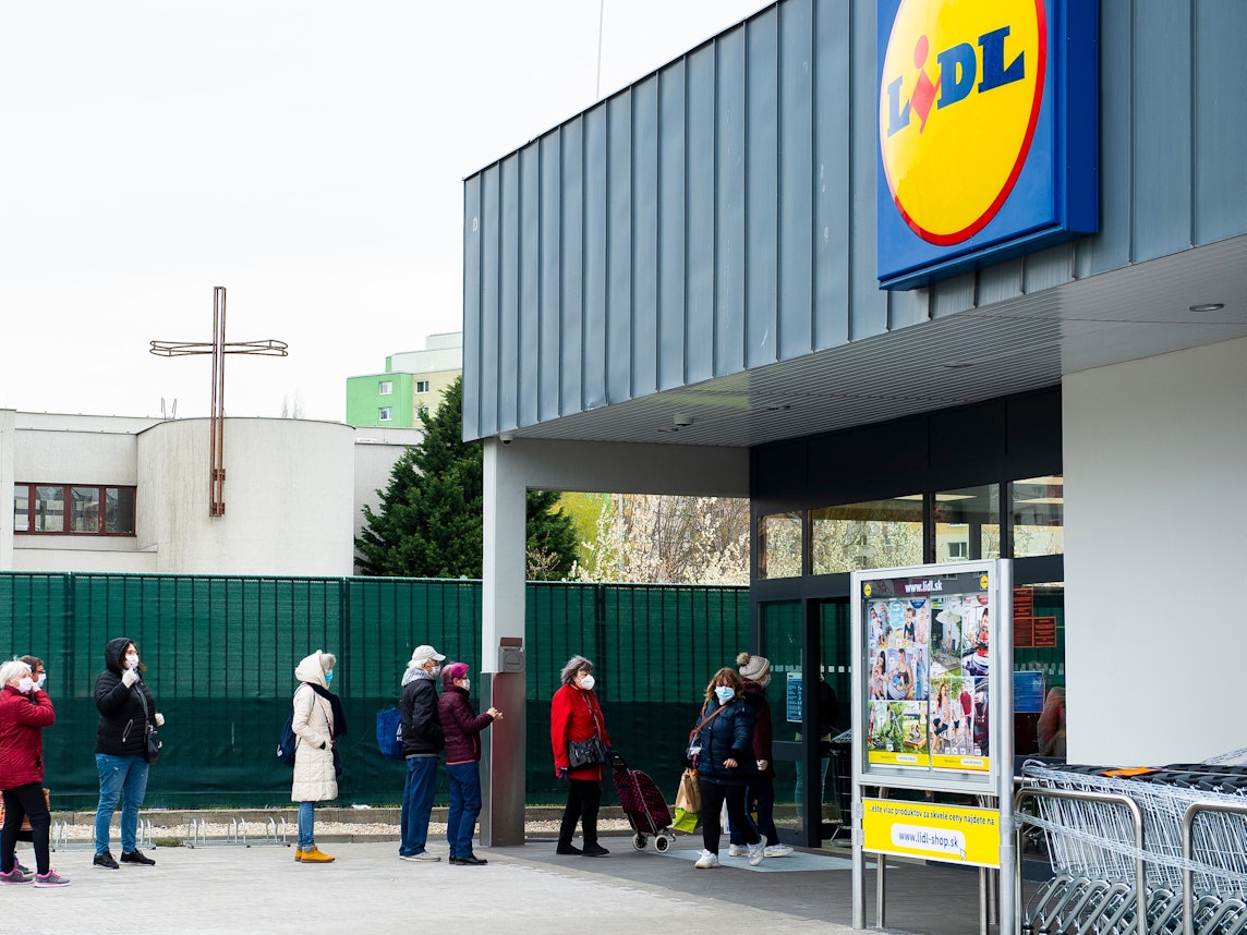 Kunden stehen mit Mundschutz und unter Einhaltung eines Sicherheitsabstandes vor einem Lidl Supermarkt Schlange.