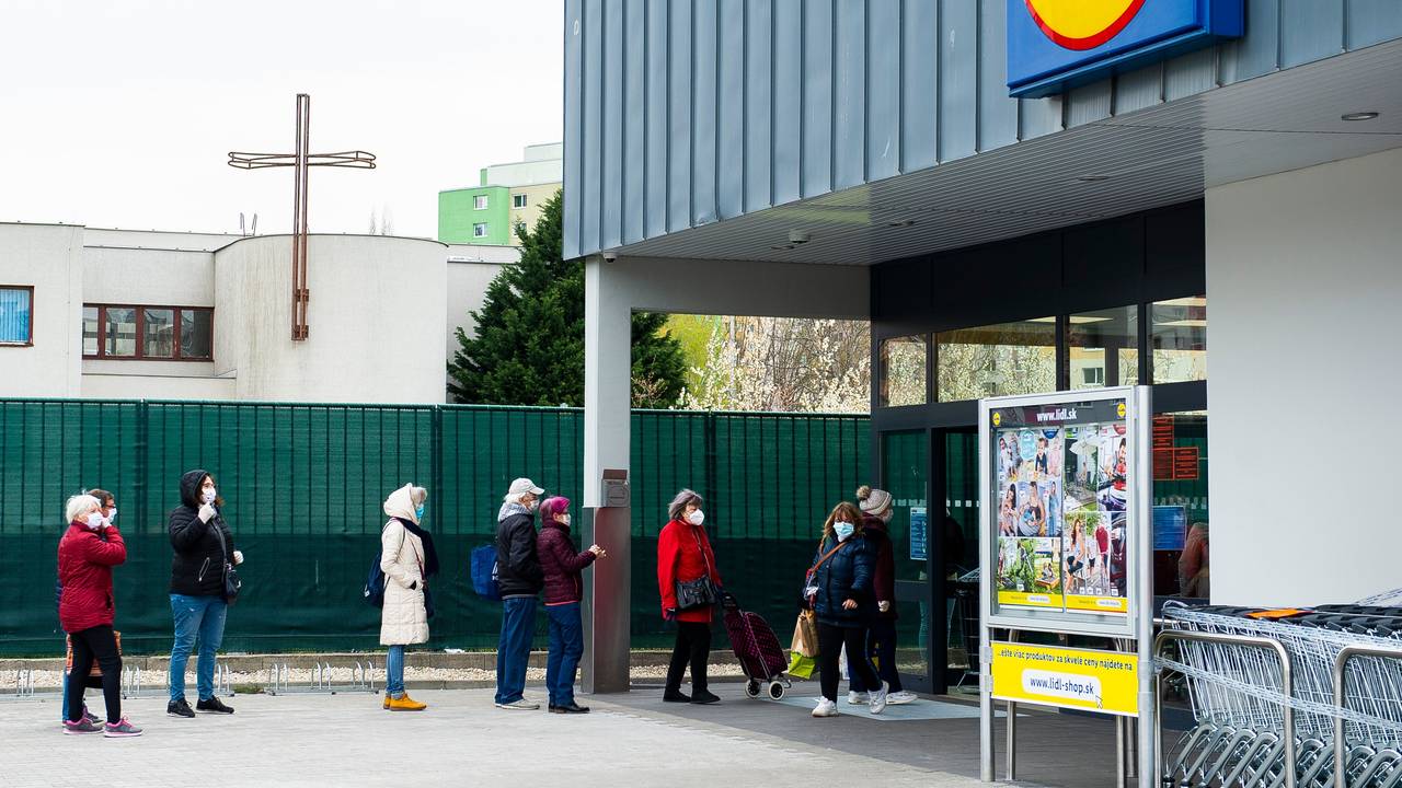 Kunden stehen mit Mundschutz und unter Einhaltung eines Sicherheitsabstandes vor einem Lidl Supermarkt Schlange.