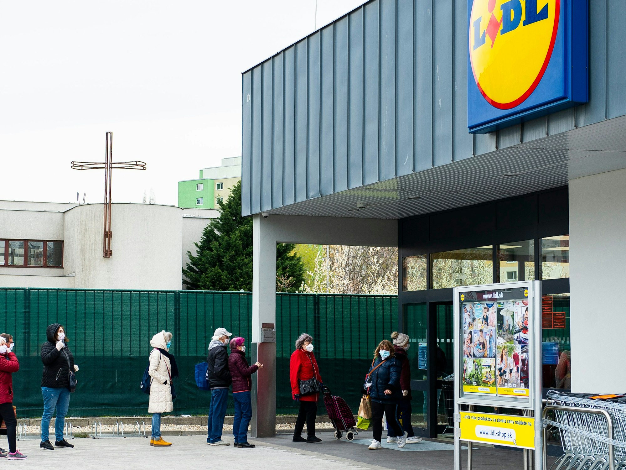 Kunden stehen mit Mundschutz und unter Einhaltung eines Sicherheitsabstandes vor einem Lidl Supermarkt Schlange.