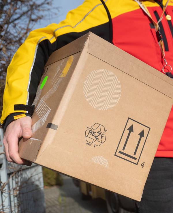 Das Bild zeigt einen DHL-Mitarbeiter mit einem Paket unter seinem Arm.
