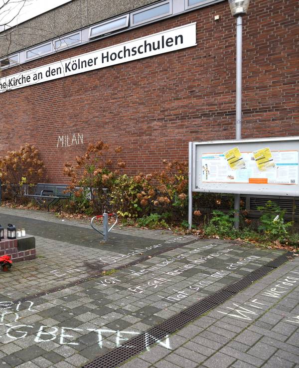 Blumen und Kerzen stehen neben einem Schriftzug auf dem Boden.