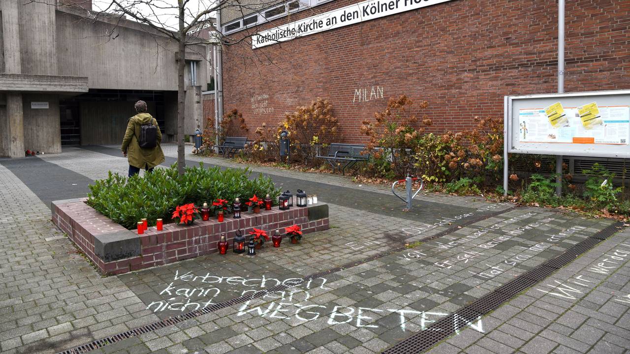 Blumen und Kerzen stehen neben einem Schriftzug auf dem Boden.