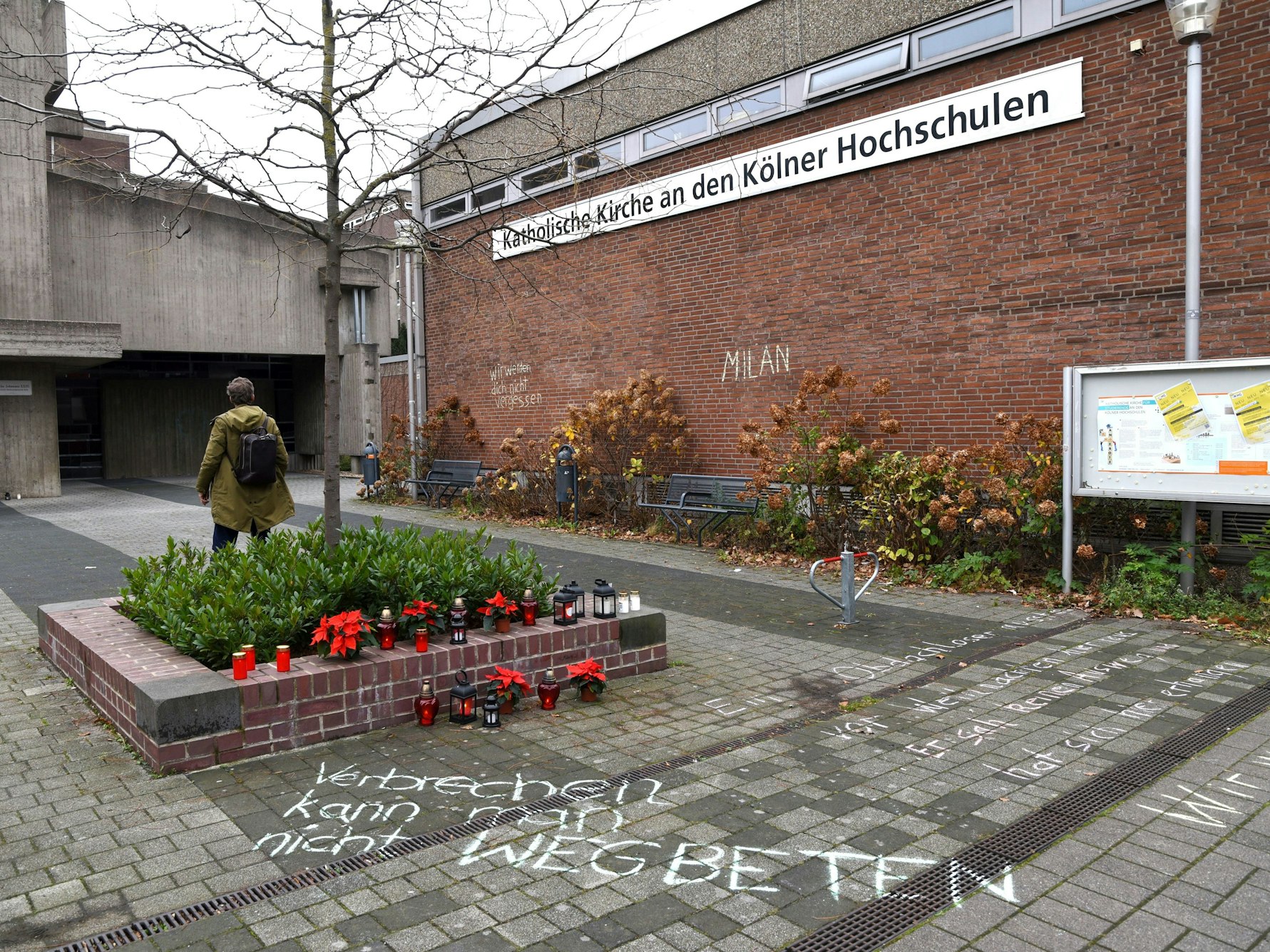 Blumen und Kerzen stehen neben einem Schriftzug auf dem Boden.