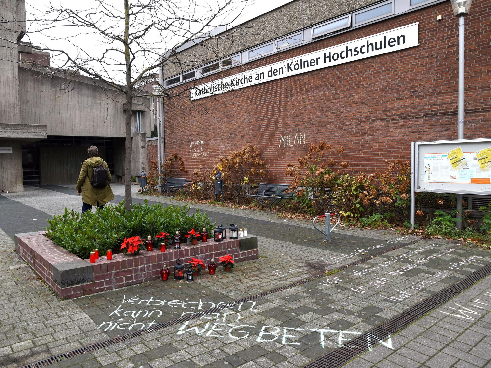 Blumen und Kerzen stehen neben einem Schriftzug auf dem Boden.