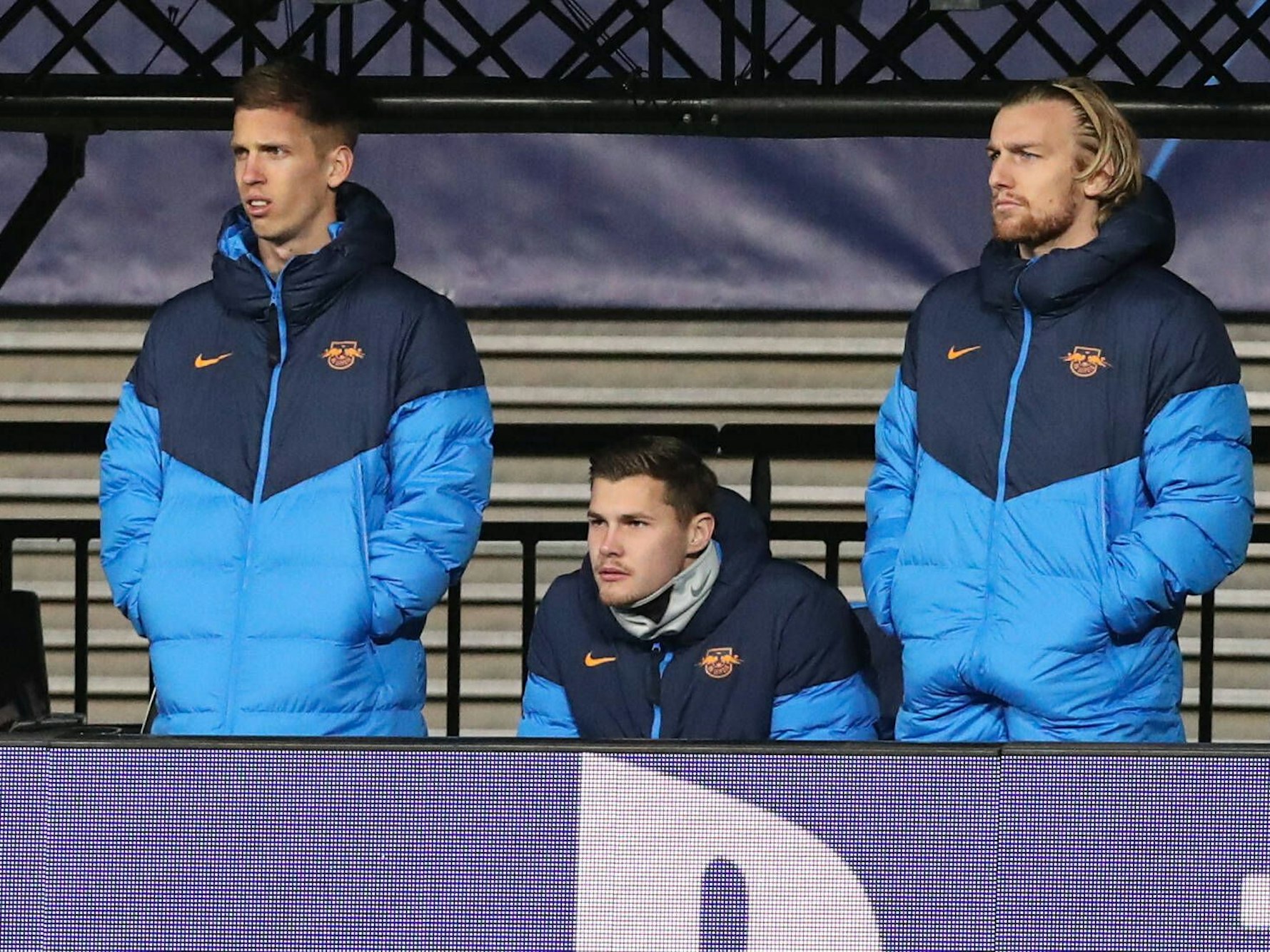 Dani Olmo, Josep Martinez und Emil Forsberg gucken in Trainingsjacken bekleidet auf das Spielfeld.