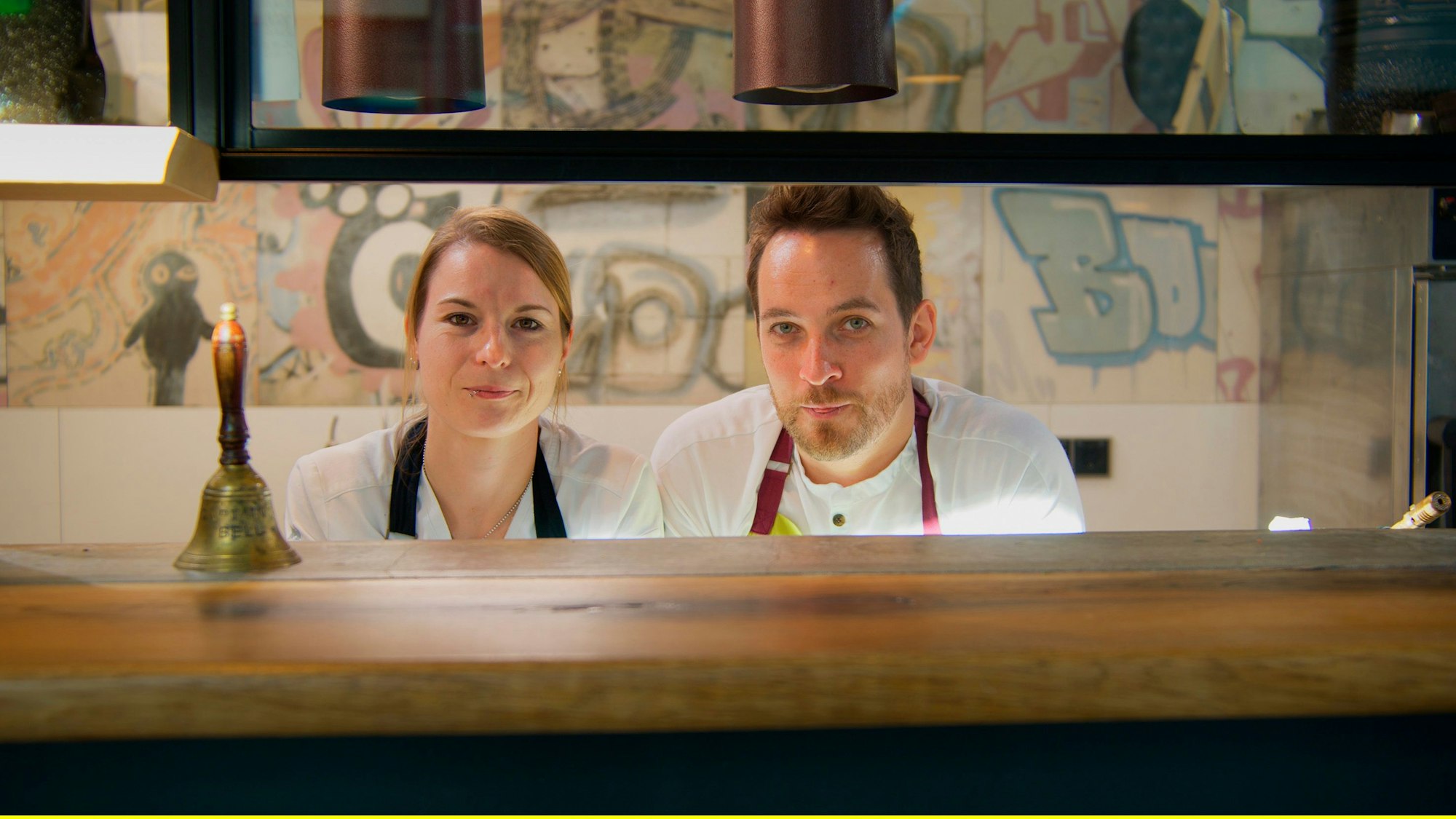 Sonja Baumann und Erik Scheffler schauen durch die Durchreiche aus der Küche.