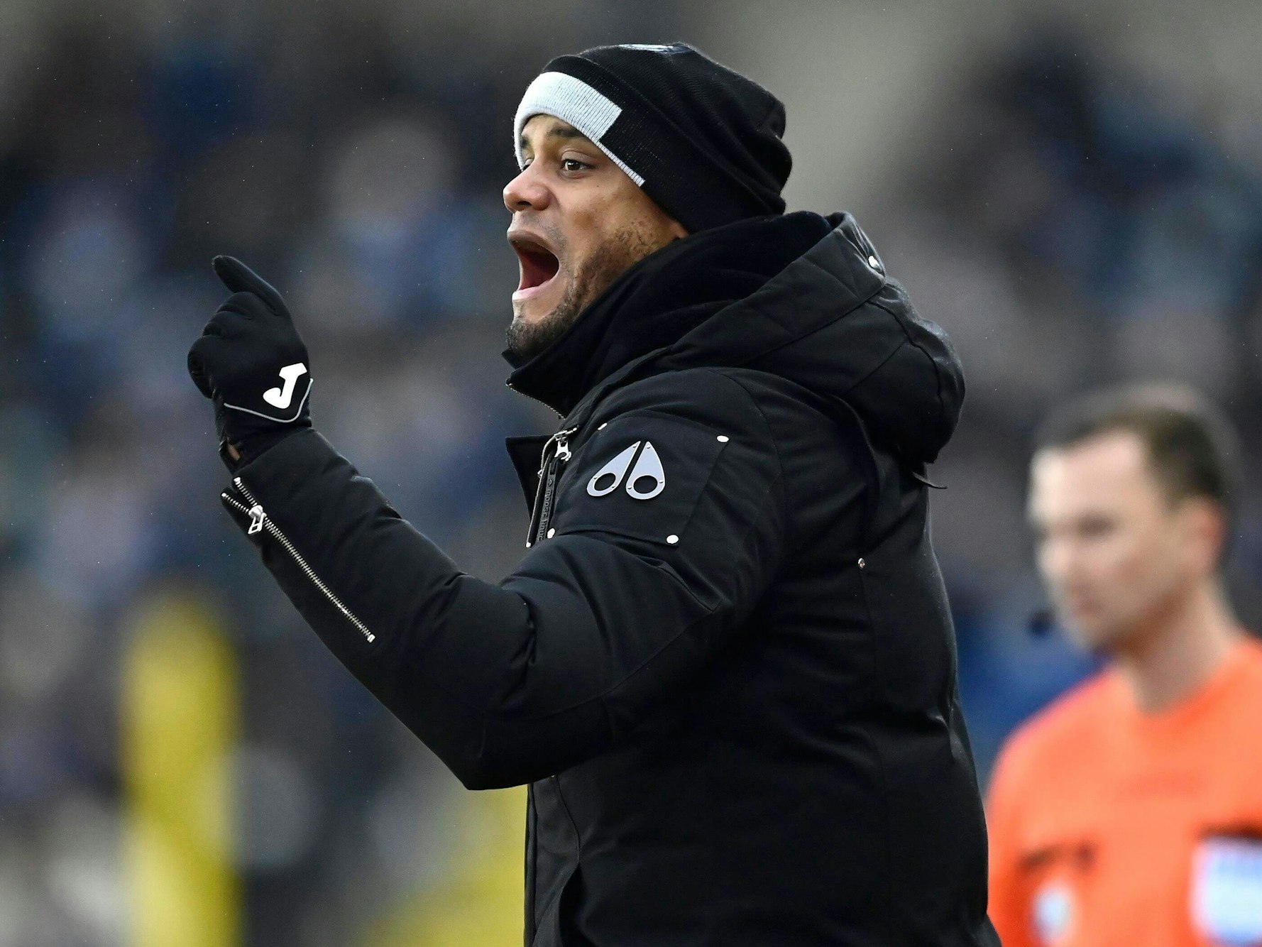 Vincent Kompany trägt eine Mütze und ruft seinen Spielern etwas zu. Dabei gestikuliert er.