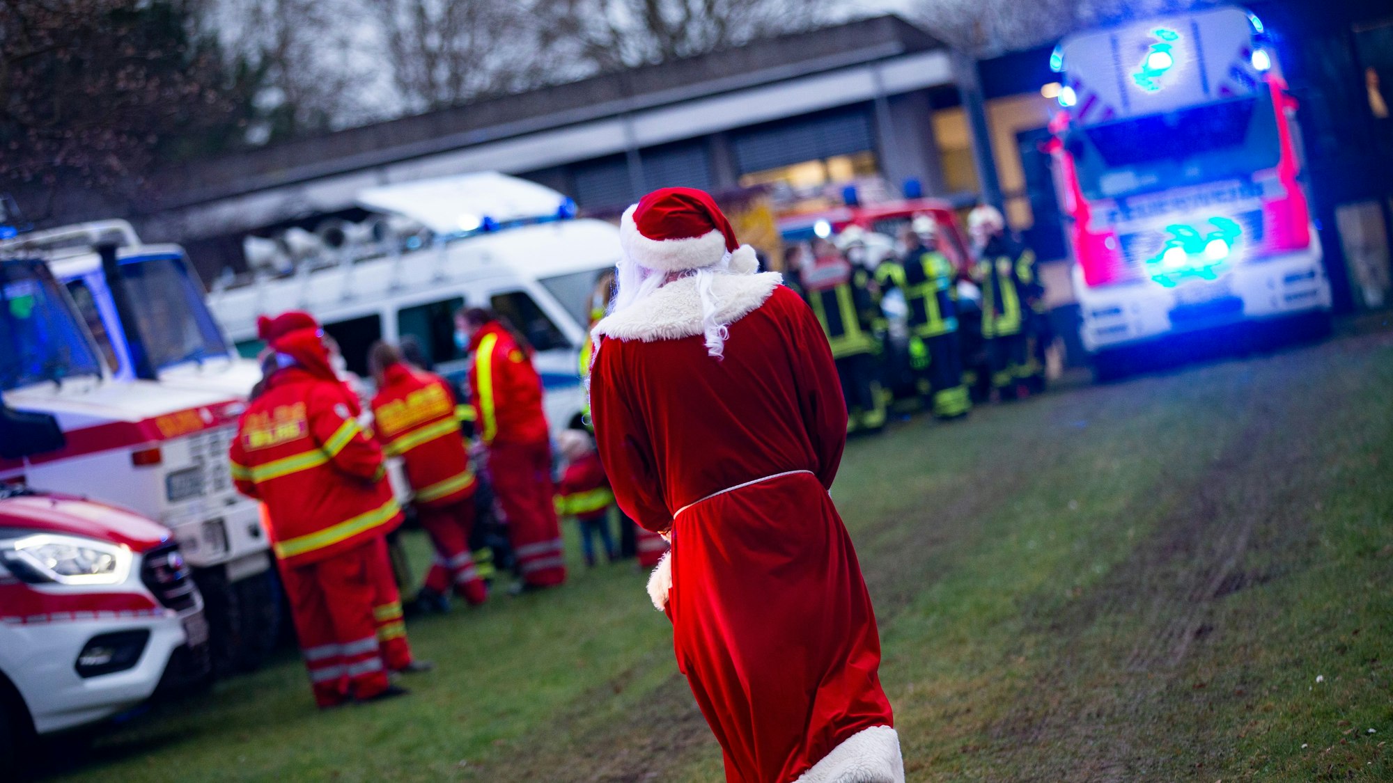 Ein verkleideter Weihnachtsmann inmitten von Einsatzwägen mit Blaulicht an der Kinderklinik des Krankenhauses in Porz