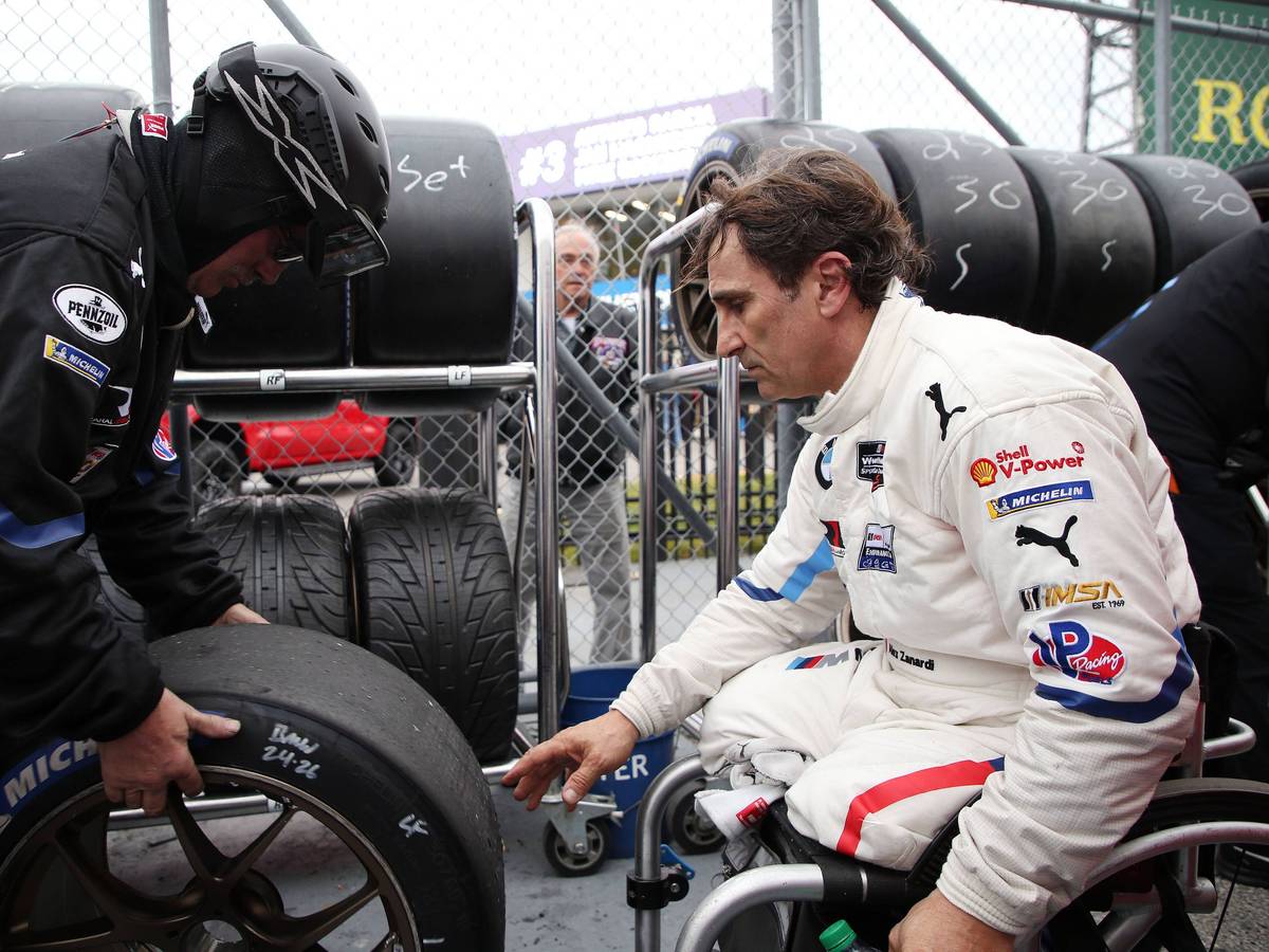 Alessandro Zanardi sitzt in Rollstuhl und greift nach einen Autoreifen.