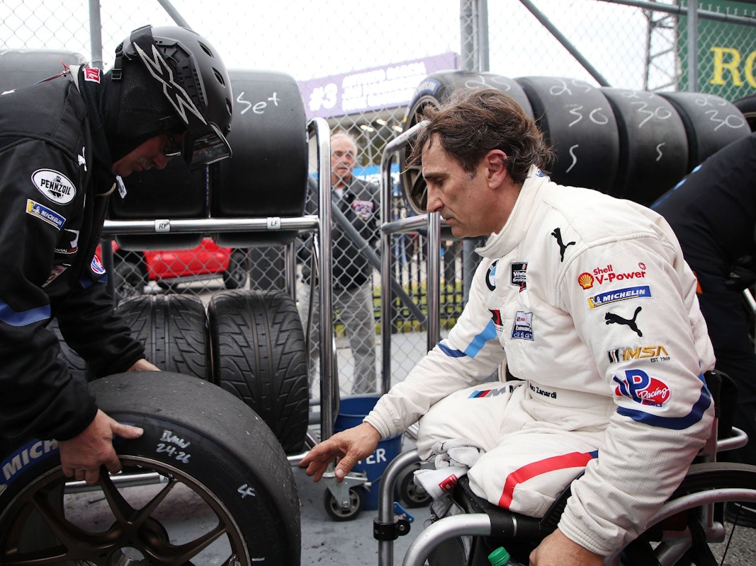 Alessandro Zanardi sitzt in Rollstuhl und greift nach einen Autoreifen.