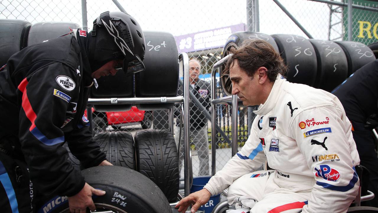 Alessandro Zanardi sitzt in Rollstuhl und greift nach einen Autoreifen.
