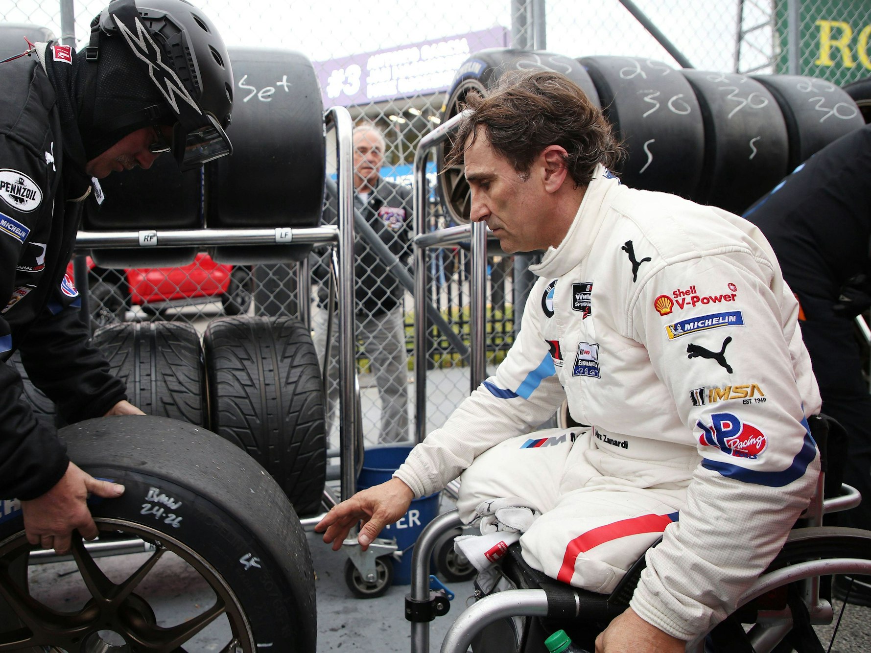 Alessandro Zanardi sitzt in Rollstuhl und greift nach einen Autoreifen.