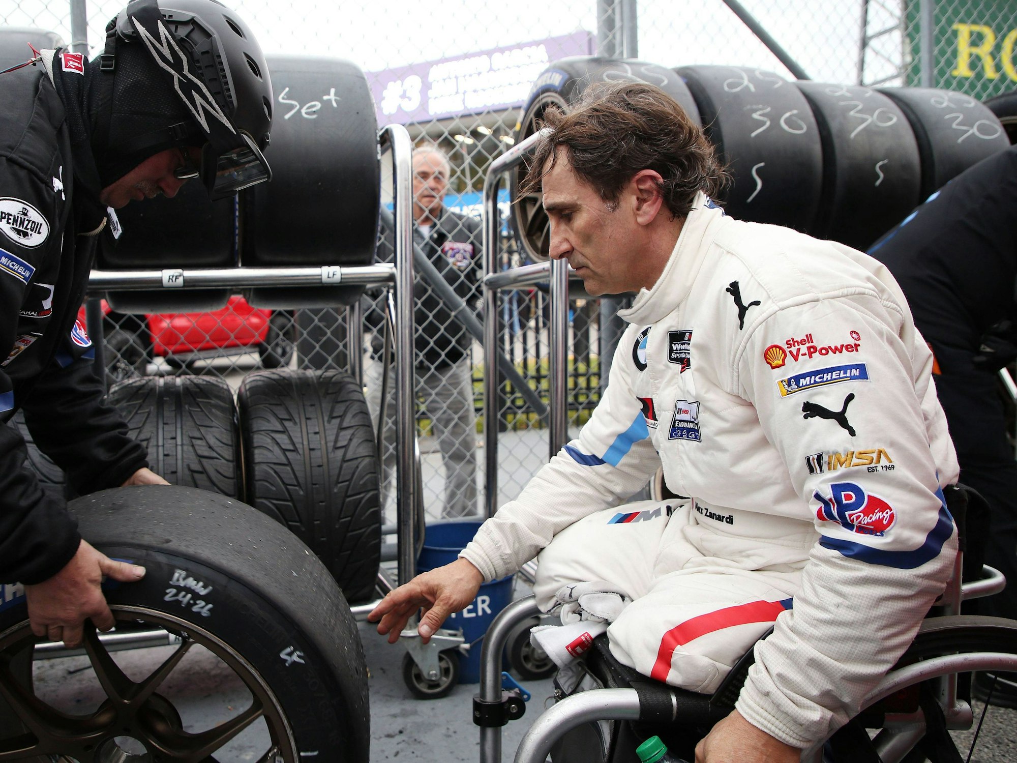 Alessandro Zanardi sitzt in Rollstuhl und greift nach einen Autoreifen.