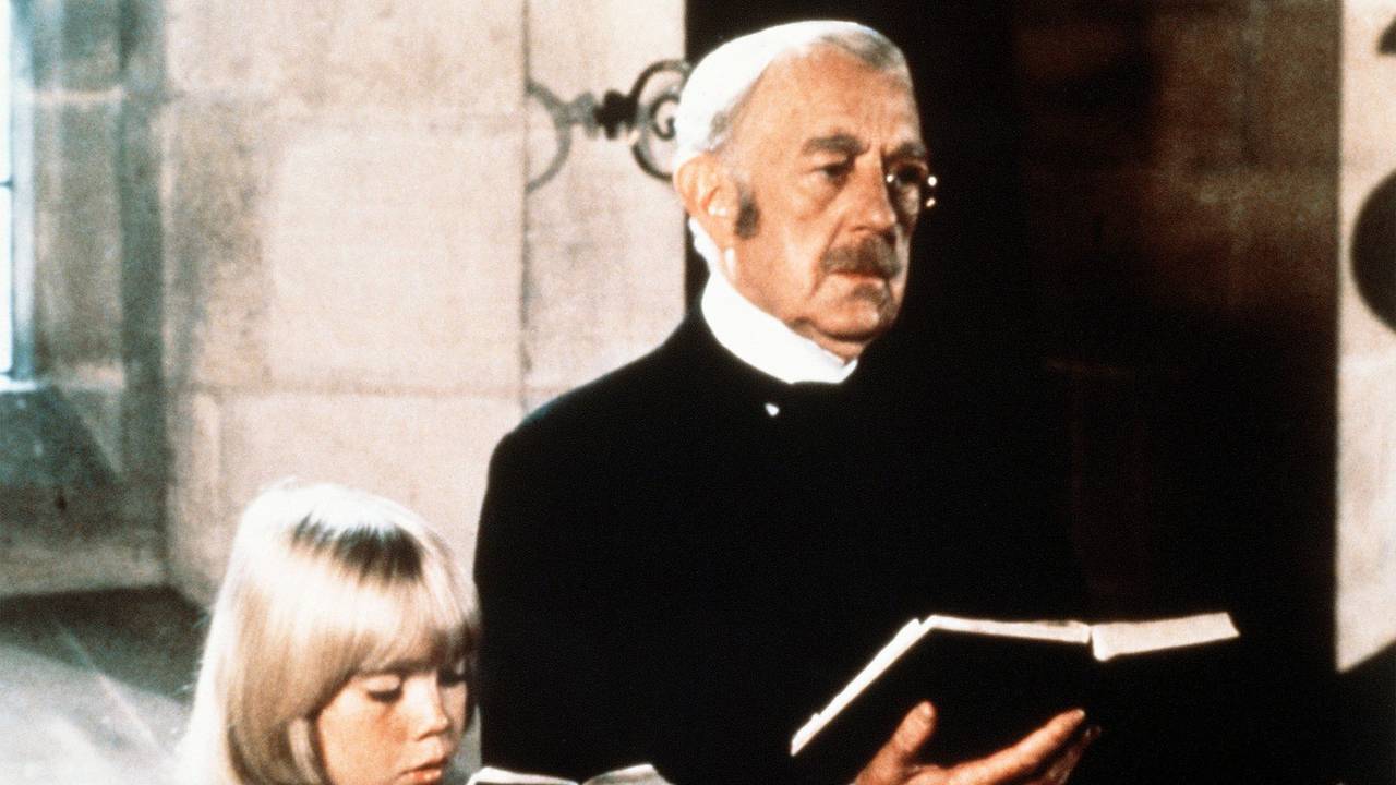 Der alte Earl of Dorincourt (Alec Guinness) steht neben seinem Enkel Ceddie (Ricky Schroder). Beide halten ein Gesangsbuch in der Hand.