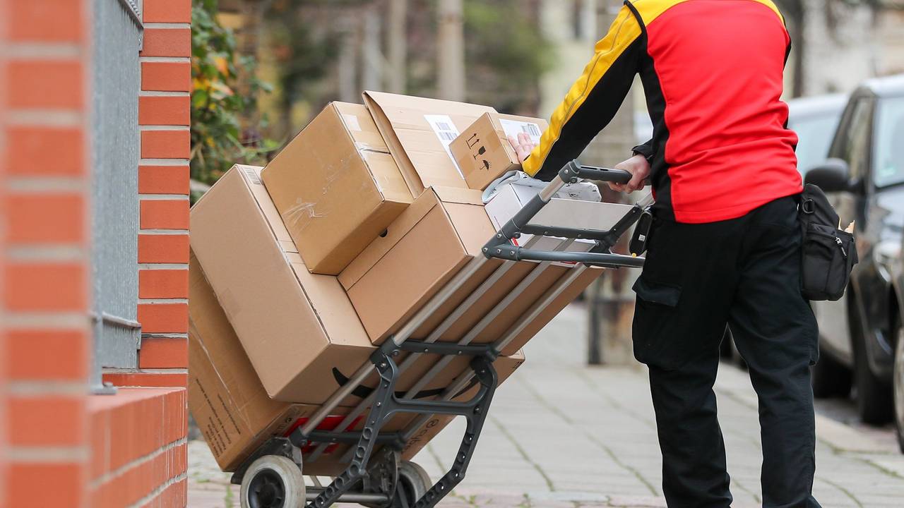 Ein Paketzusteller geht mit einer Sackkarre voller Pakete zu einem Haus.