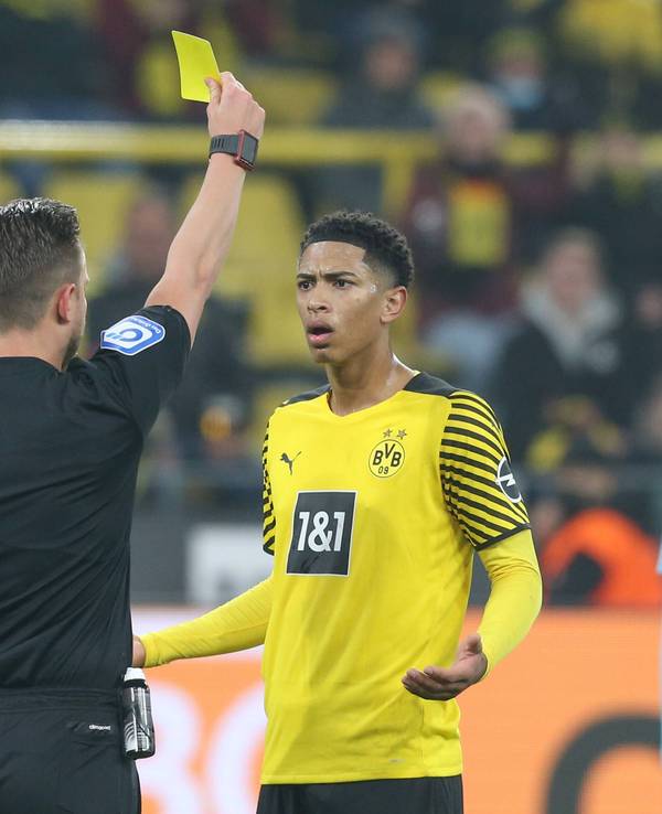 Jude Bellingham bekommt vom Schiedsrichter die Gelbe Karte. Bellingham schaut verständnislos und breitet die Arme fragend aus.