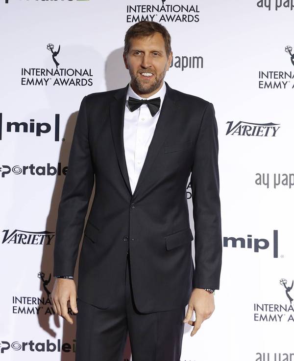 Dirk Nowitzki steht im Anzug vor einer Werbebande.