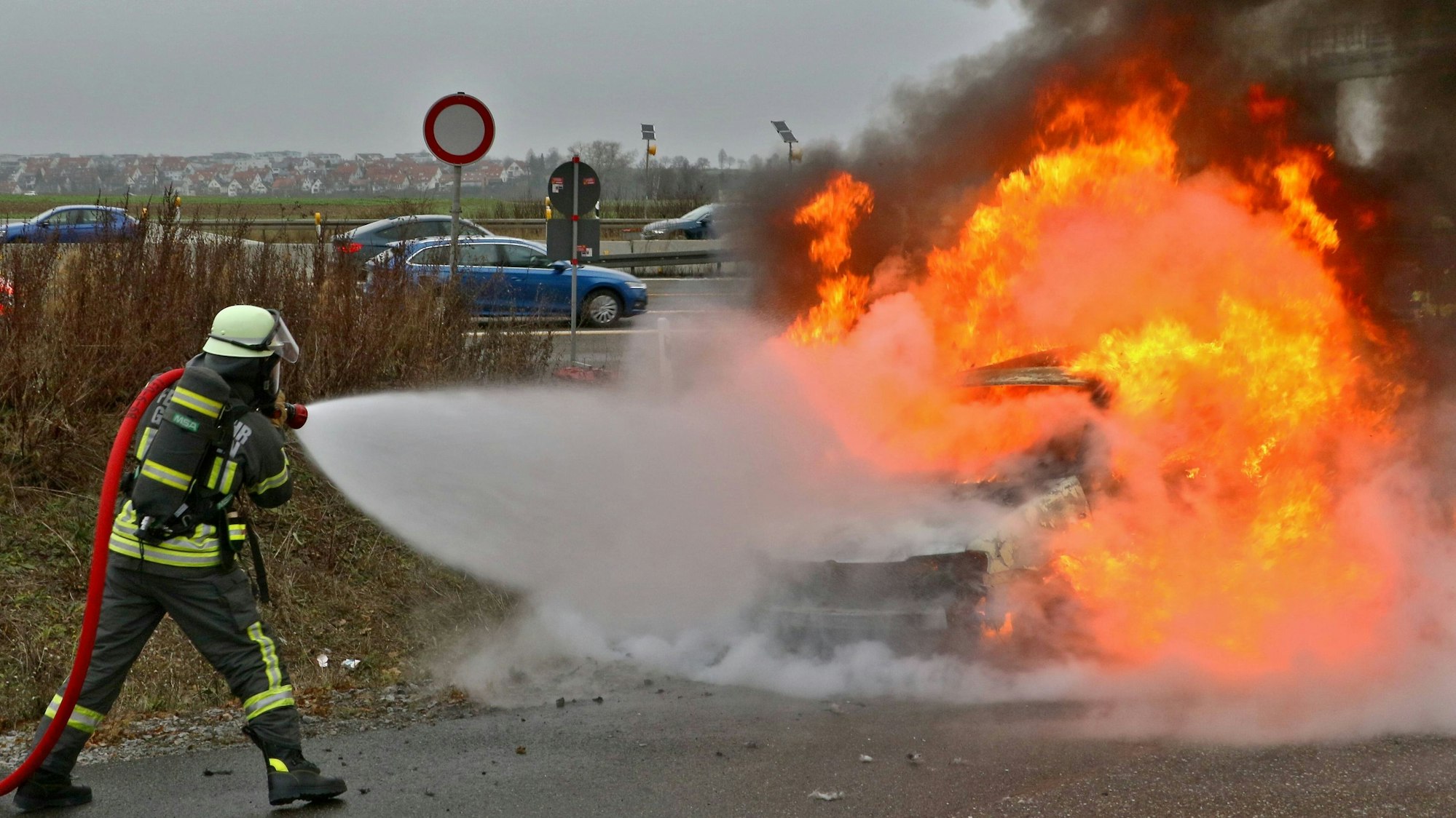 Ein Feuerwehrmann löscht mit einen Wasserschlauch einen Wagen, der in Flammen steht.