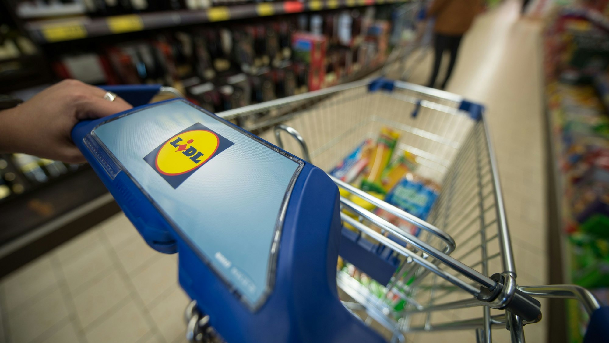 Eine Frau schiebt in einer Filiale des Lebensmitteldiscounters Lidl einen Einkaufswagen durch die Regalreihen.