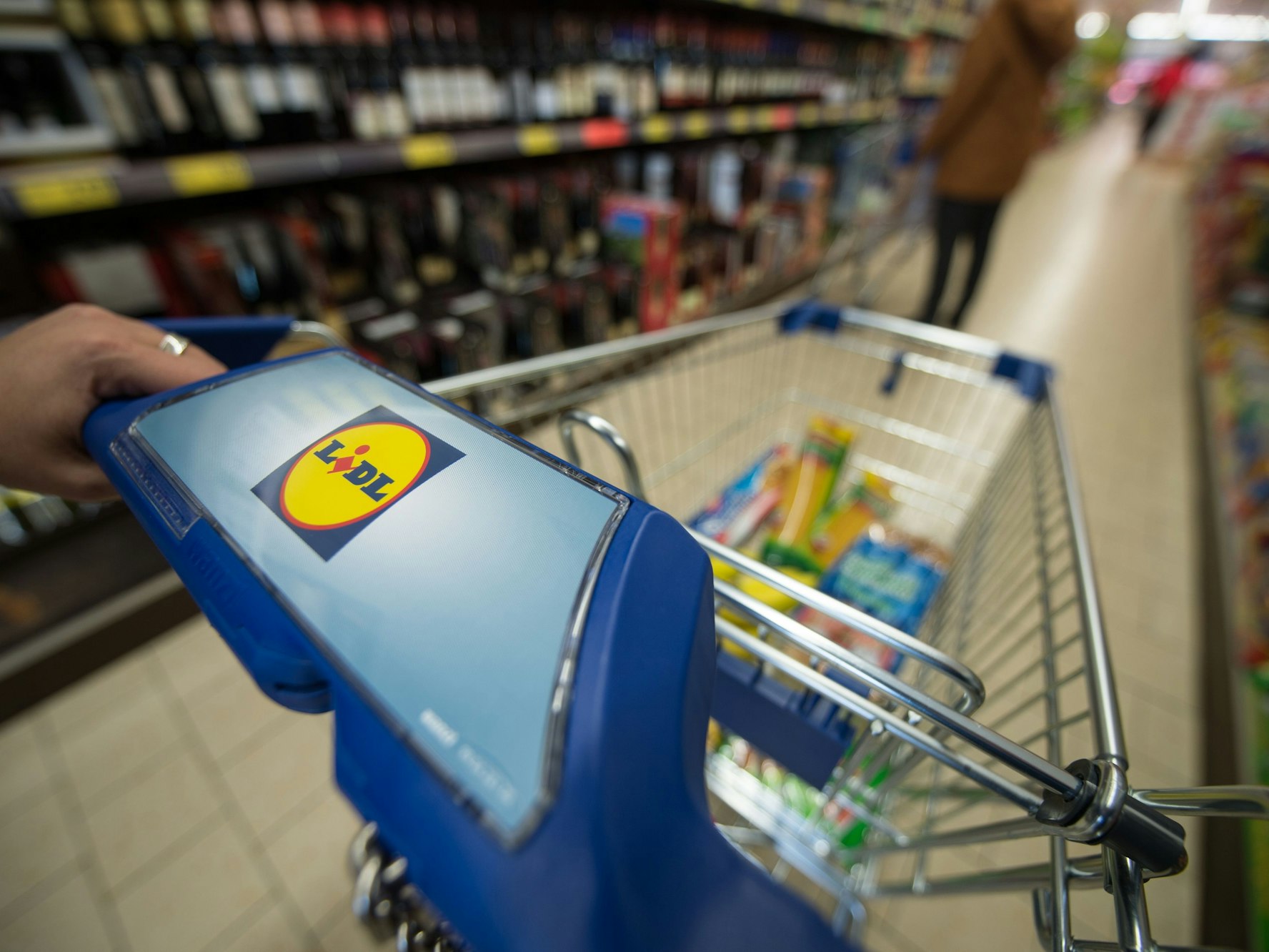 Eine Kundin schiebt einen Einkaufswagen durch einen Supermarkt.