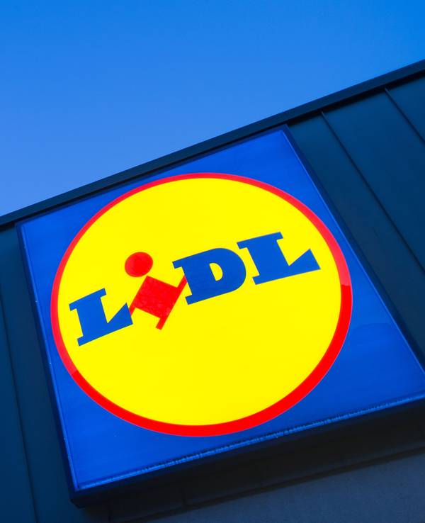 Das Logo eines Lidl-Supermarktes in Berlin-Reinickendorf leuchtet vor dem Abendhimmel.