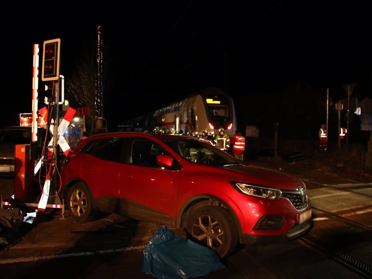 Ein Auto steht neben einer Schrankenanlage, im Hintergrund der ICE