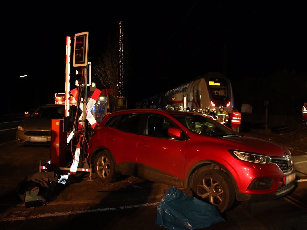 Ein Auto steht neben einer Schrankenanlage, im Hintergrund der ICE